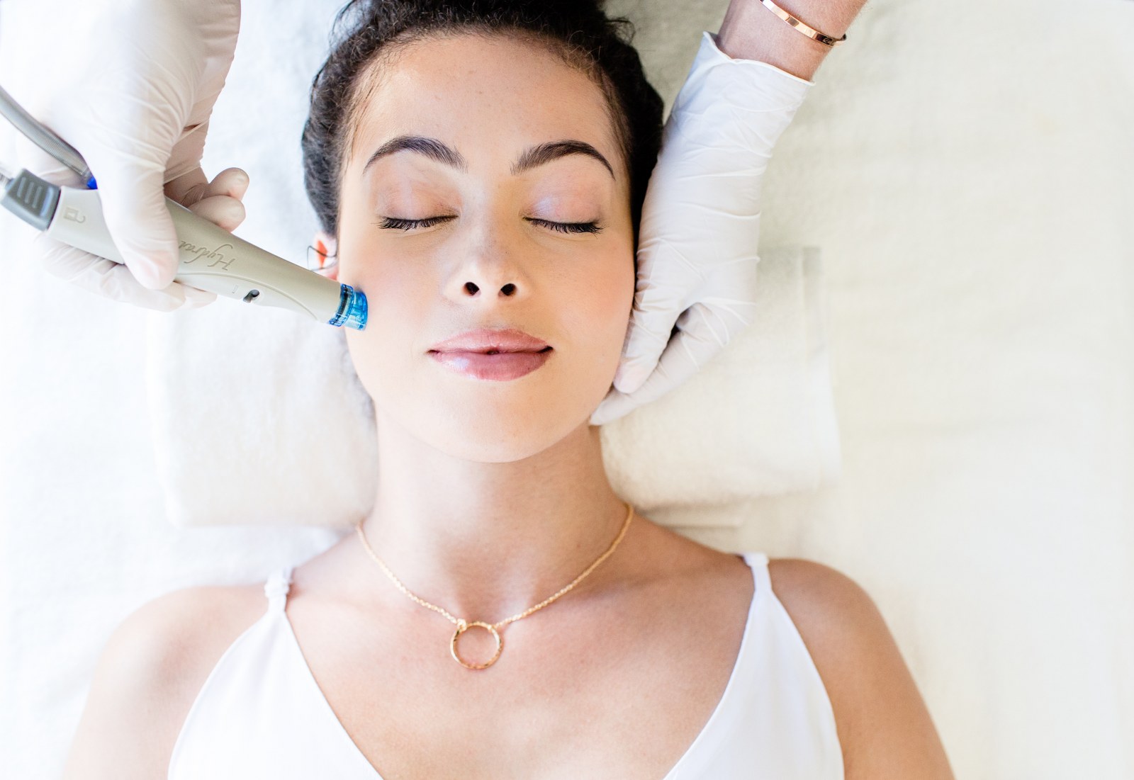 Woman having a hydrafacial treatment applied to the cheek of her face.