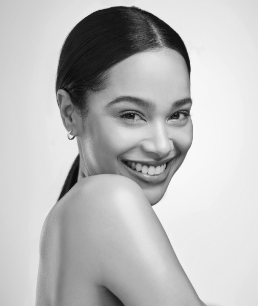 Black and white portrait of a woman with sleek hair pulled back, smiling warmly at the camera. She is turned slightly to the side and exudes confidence and joy. The plain background emphasizes her facial features and smooth skin, a testament to effective skin care in Wake County.
