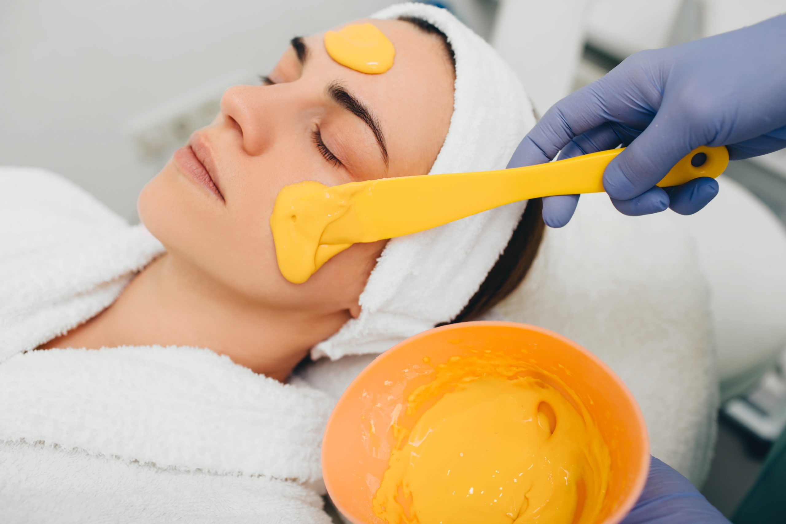 A person gets a yellow facial mask applied with a spatula during Skincare Services Wake County, NC.
